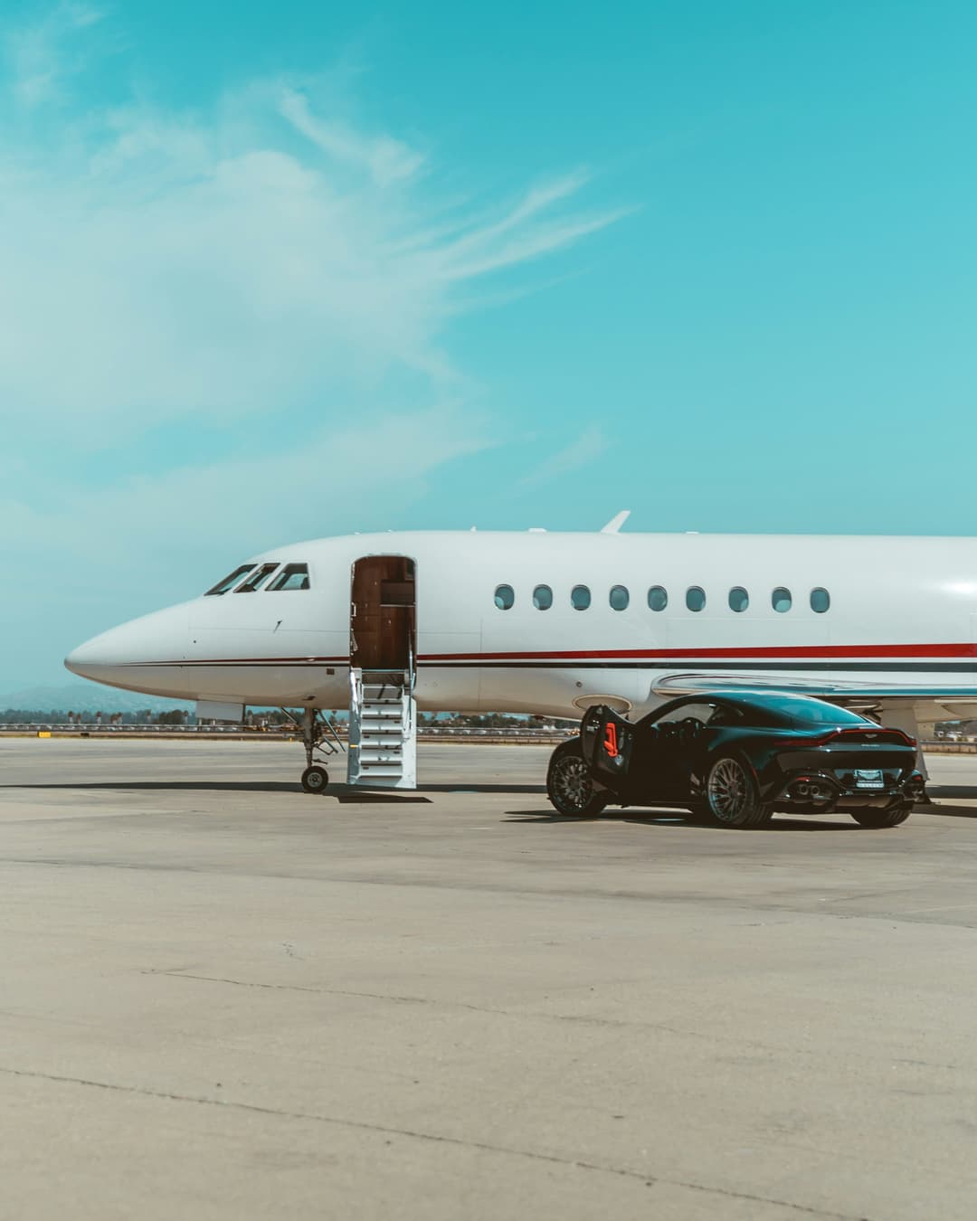 Business jet parked on the apron beside a sports car